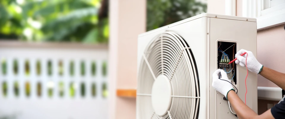 Technicien en combinaison blanche effectuant la maintenance d'une unité extérieure de climatisation sur terrasse ensoleillée